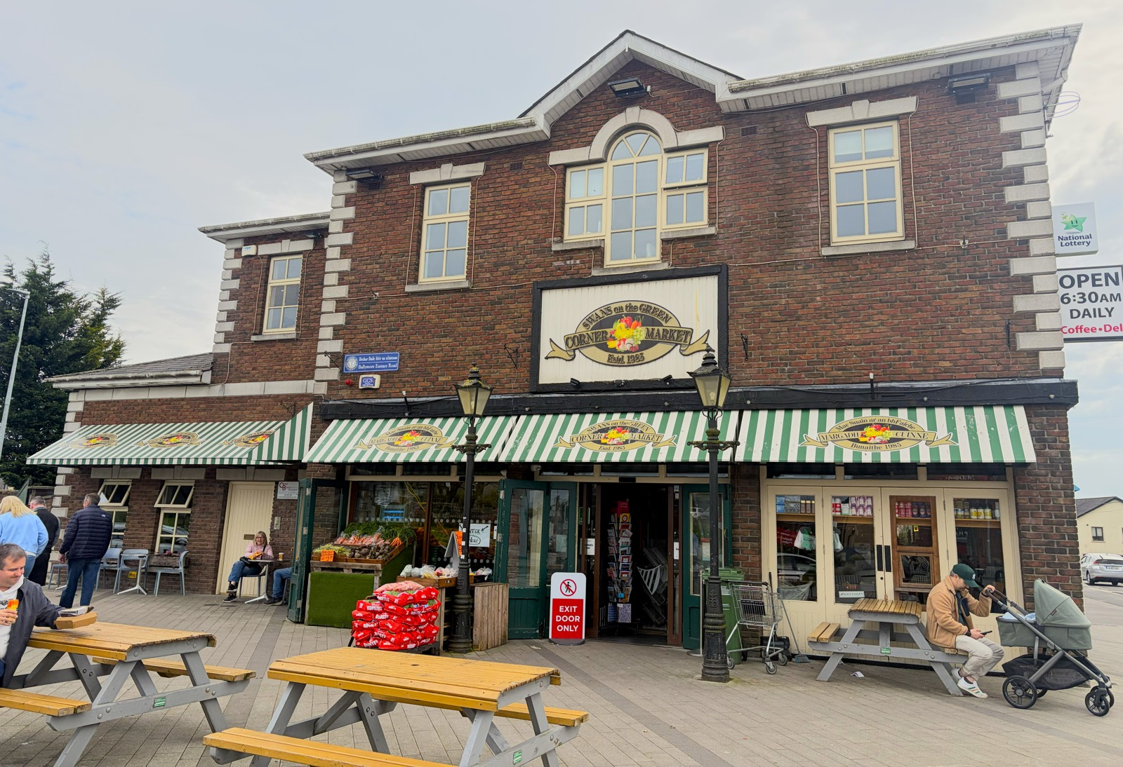 The red-brick shopfront of Swans on the Green, with green-and-white striped awnings, old lamp posts and picnic benches out front